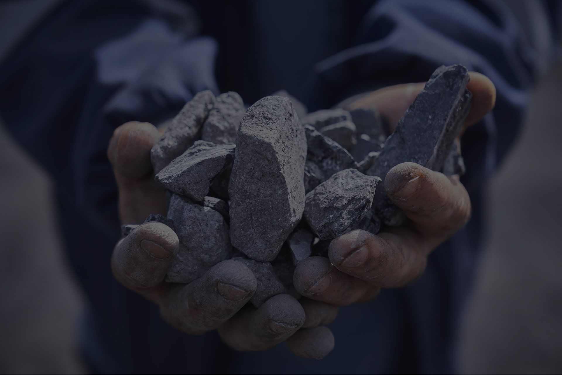 A person holding rough, gray rocks in cupped hands, showcasing raw minerals or stones.