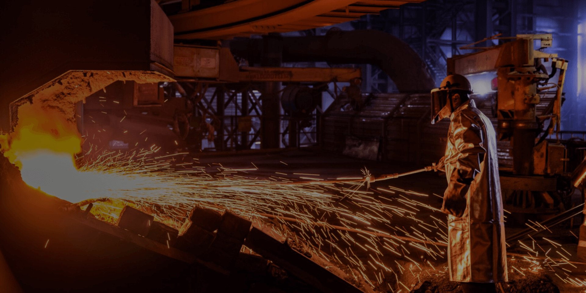 Industrial worker in protective gear managing molten metal in a steel foundry with sparks flying.